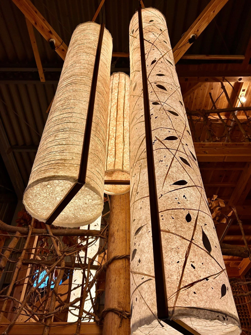 Decorative washi cylindrical lights with leaf patterns hanging from a wooden ceiling.