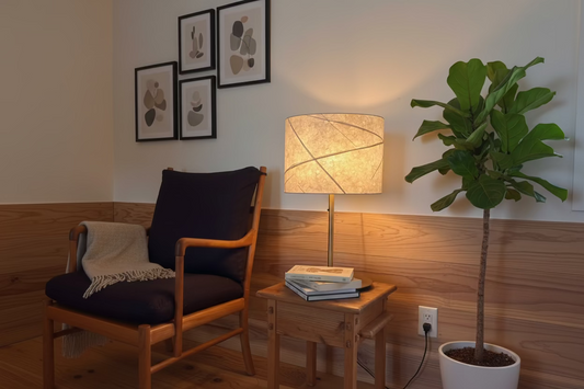 Wooden chair with dark cushion next to a handcrafted washi lamp on a wooden table against a light wall.