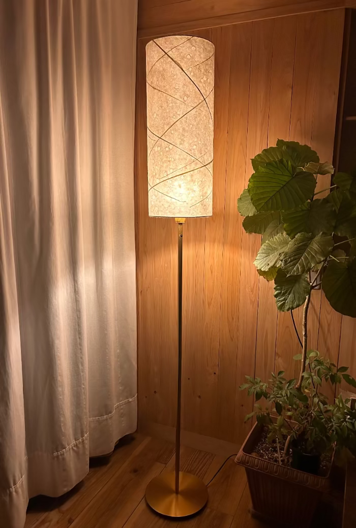 Floor lamp with a textured washi lampshade in a room with wooden walls and a plant.