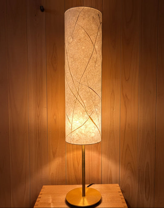 Table lamp with a cylindrical shade on a wooden surface against a wooden wall.
