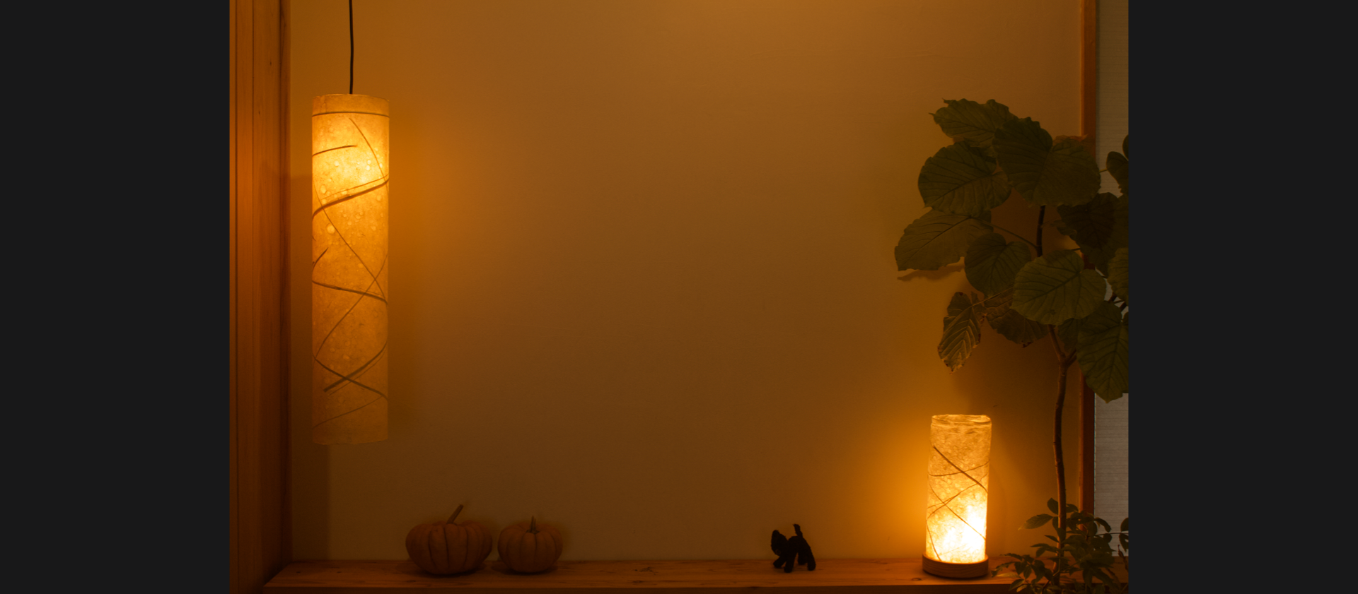 Two washi lamps with woven designs, hanging from the ceiling and sitting on a table, casting a warm glow in the room
