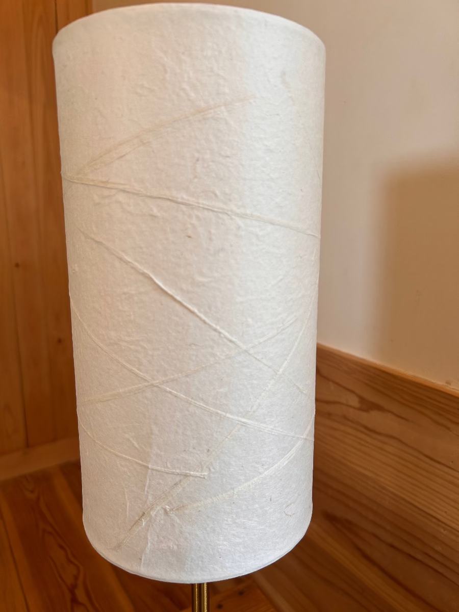 White handmade washi lampshade on a wooden stand against a wooden wall.