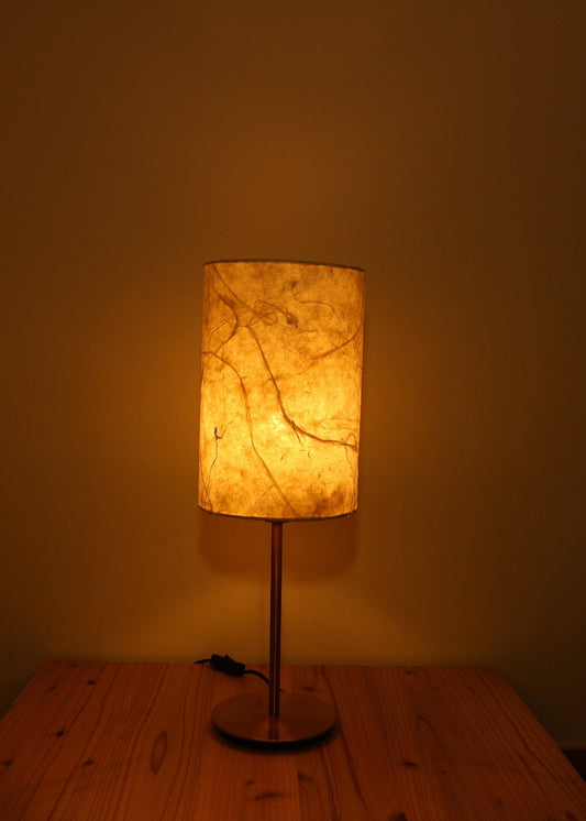 Table lamp with a textured japanese paper lampshade on a wooden table against a plain wall.